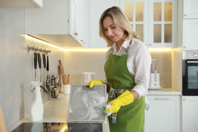 Photo of Woman cleaning filter of kitchen hood with sponge at countertop indoors