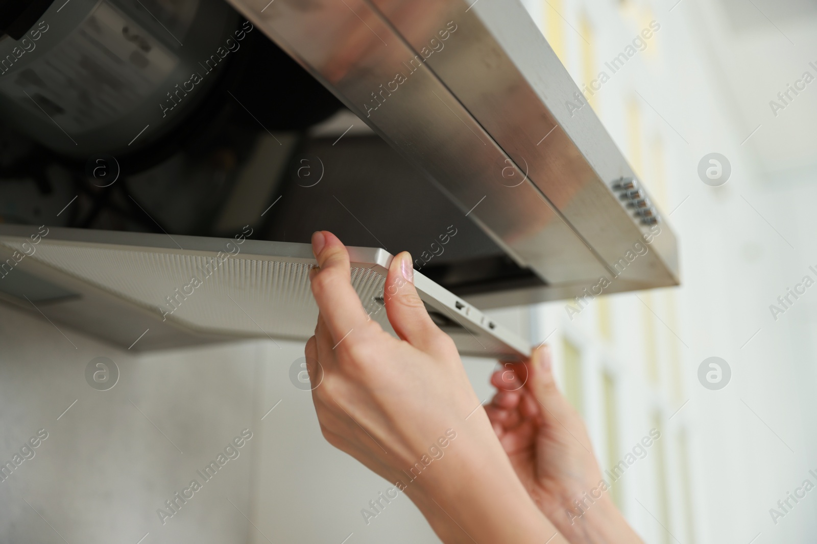 Photo of Woman removing filter from kitchen hood for cleaning indoors, closeup