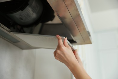 Photo of Woman removing filter from kitchen hood for cleaning indoors, closeup