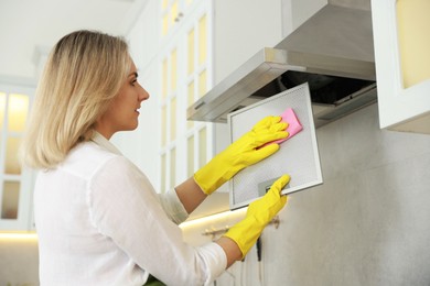 Woman cleaning filter of kitchen hood with rag indoors