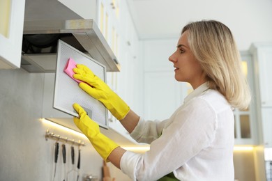 Woman cleaning filter of kitchen hood with rag indoors