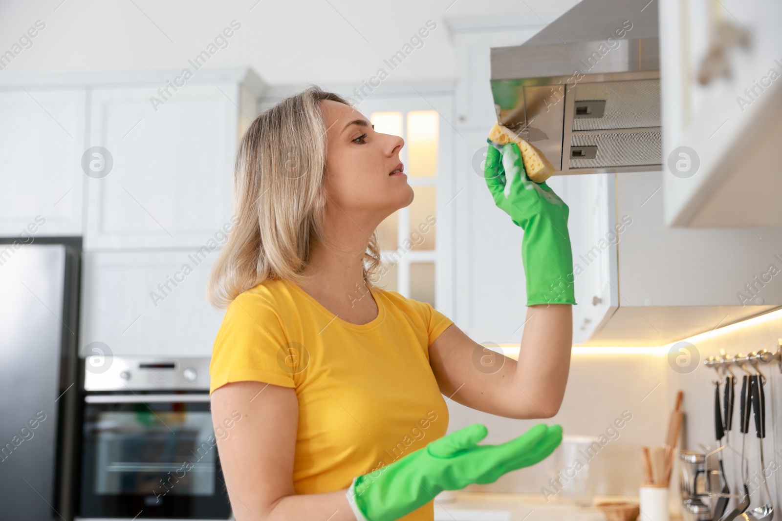 Photo of Woman cleaning kitchen hood with sponge indoors