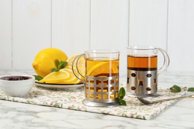 Photo of Glasses of tea in metal holders served on white marble table