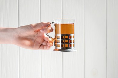 Photo of Woman with glass of tea in metal holder on white wooden background, closeup