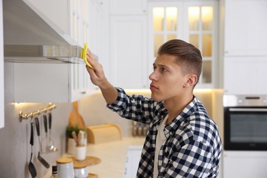 Man cleaning kitchen hood with rag at home