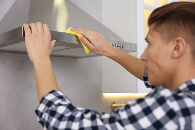 Photo of Man cleaning kitchen hood with rag at home