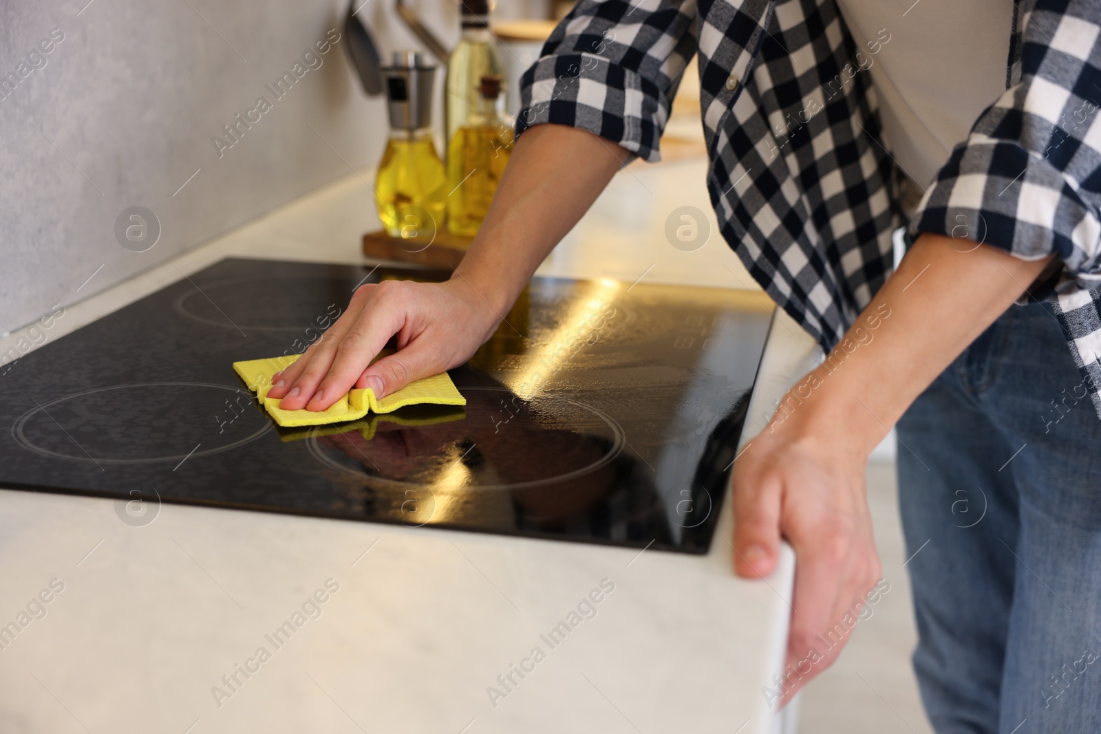 Photo of Man cleaning electric stove with rag in kitchen, closeup