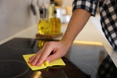 Man cleaning electric stove with rag in kitchen, closeup