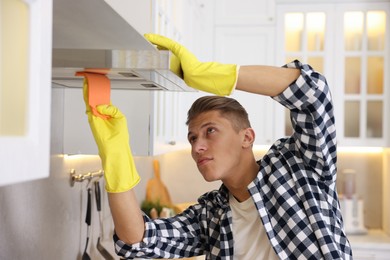 Photo of Man cleaning kitchen hood with rag at home