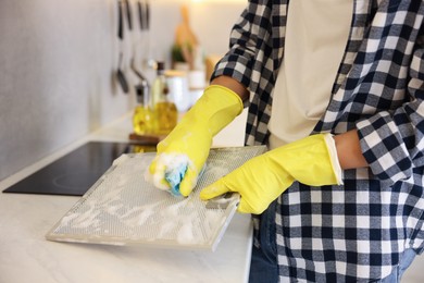 Photo of Man cleaning filter of kitchen hood with sponge indoors, closeup