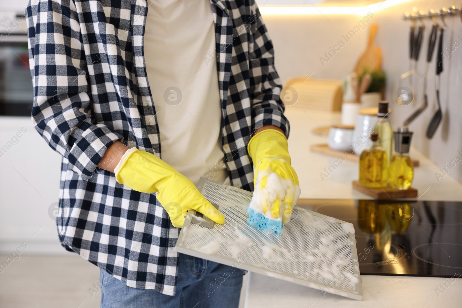 Photo of Man cleaning filter of kitchen hood with sponge indoors, closeup