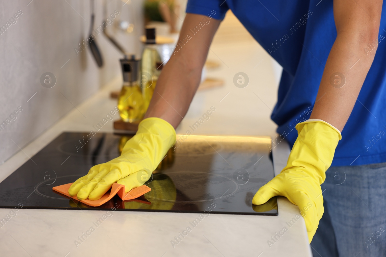 Photo of Professional janitor cleaning electric stove with rag in kitchen, closeup