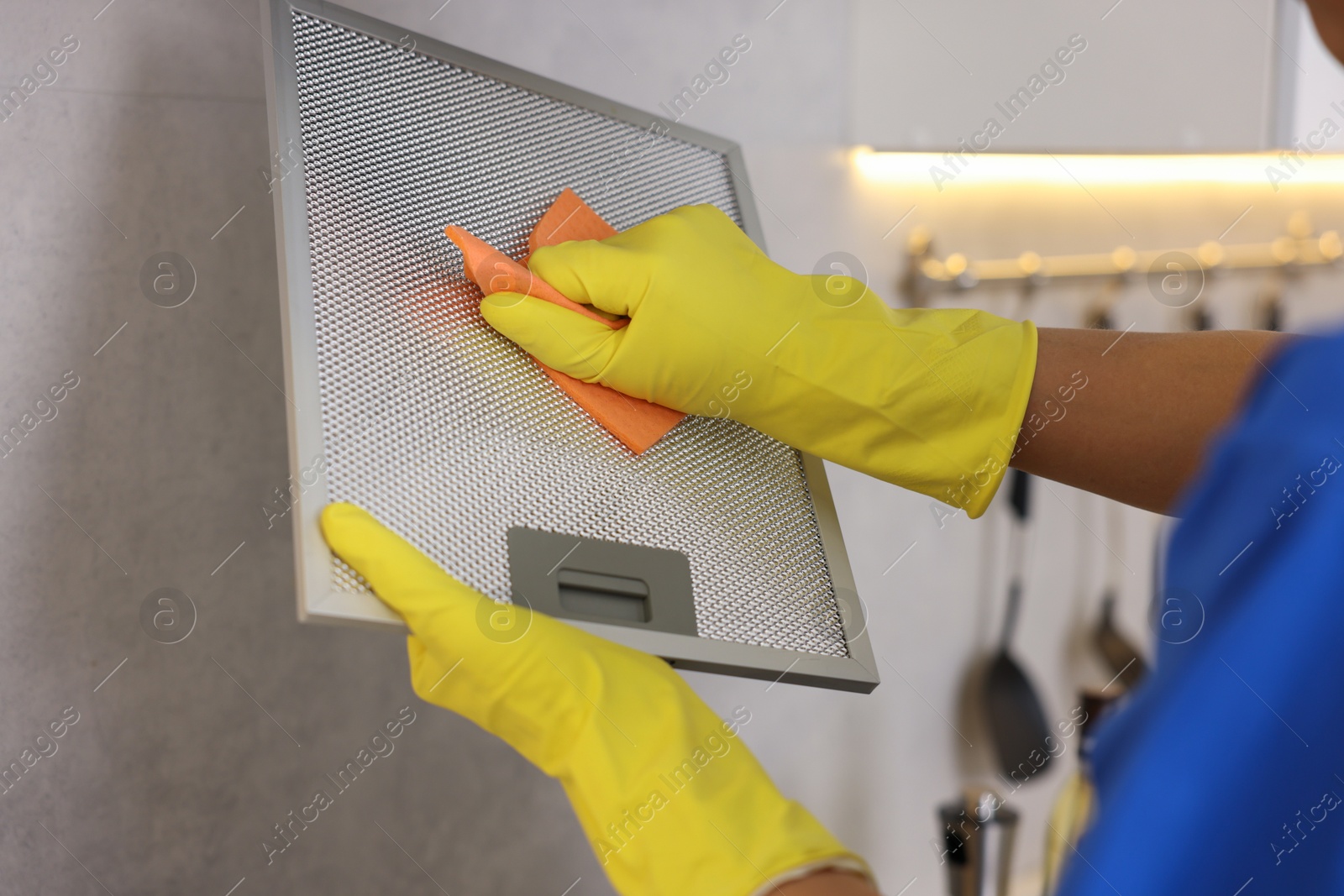 Photo of Professional janitor cleaning filter of kitchen hood with rag indoors, closeup