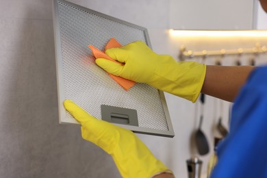 Photo of Professional janitor cleaning filter of kitchen hood with rag indoors, closeup