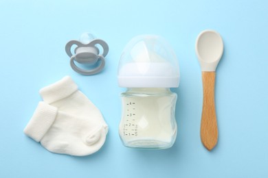 Photo of Feeding bottle with milk, baby socks, spoon and pacifier on light blue background, flat lay