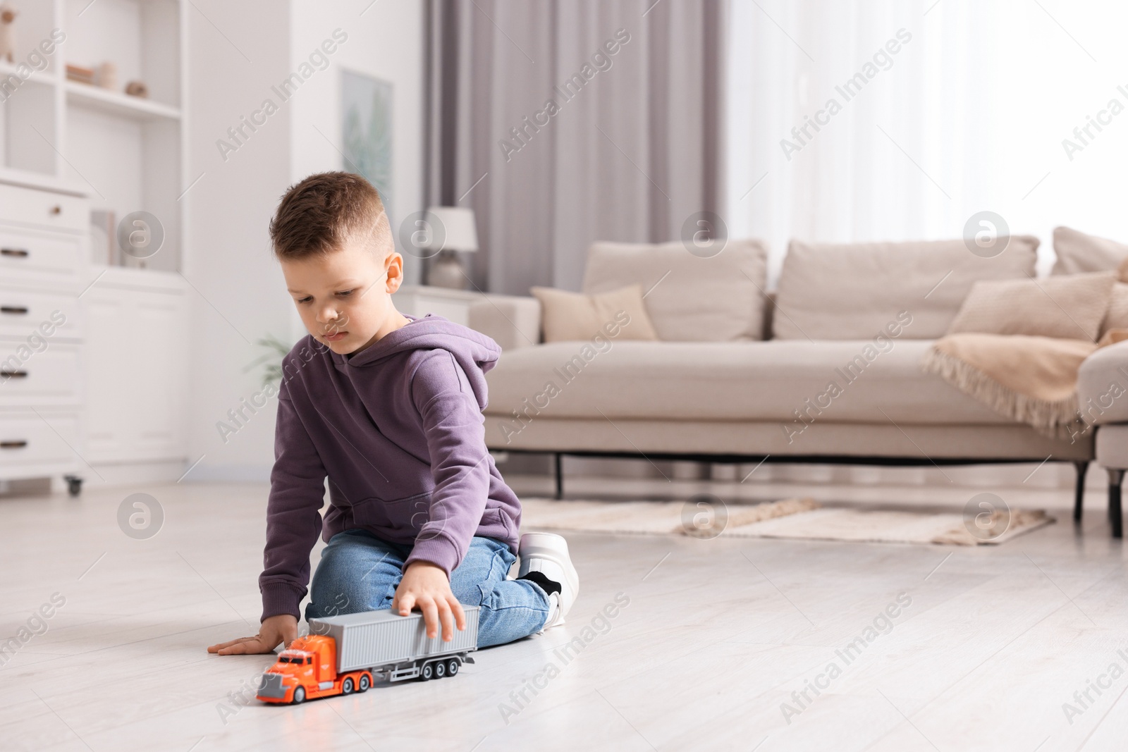 Photo of Little boy playing with toy car at home. Space for text