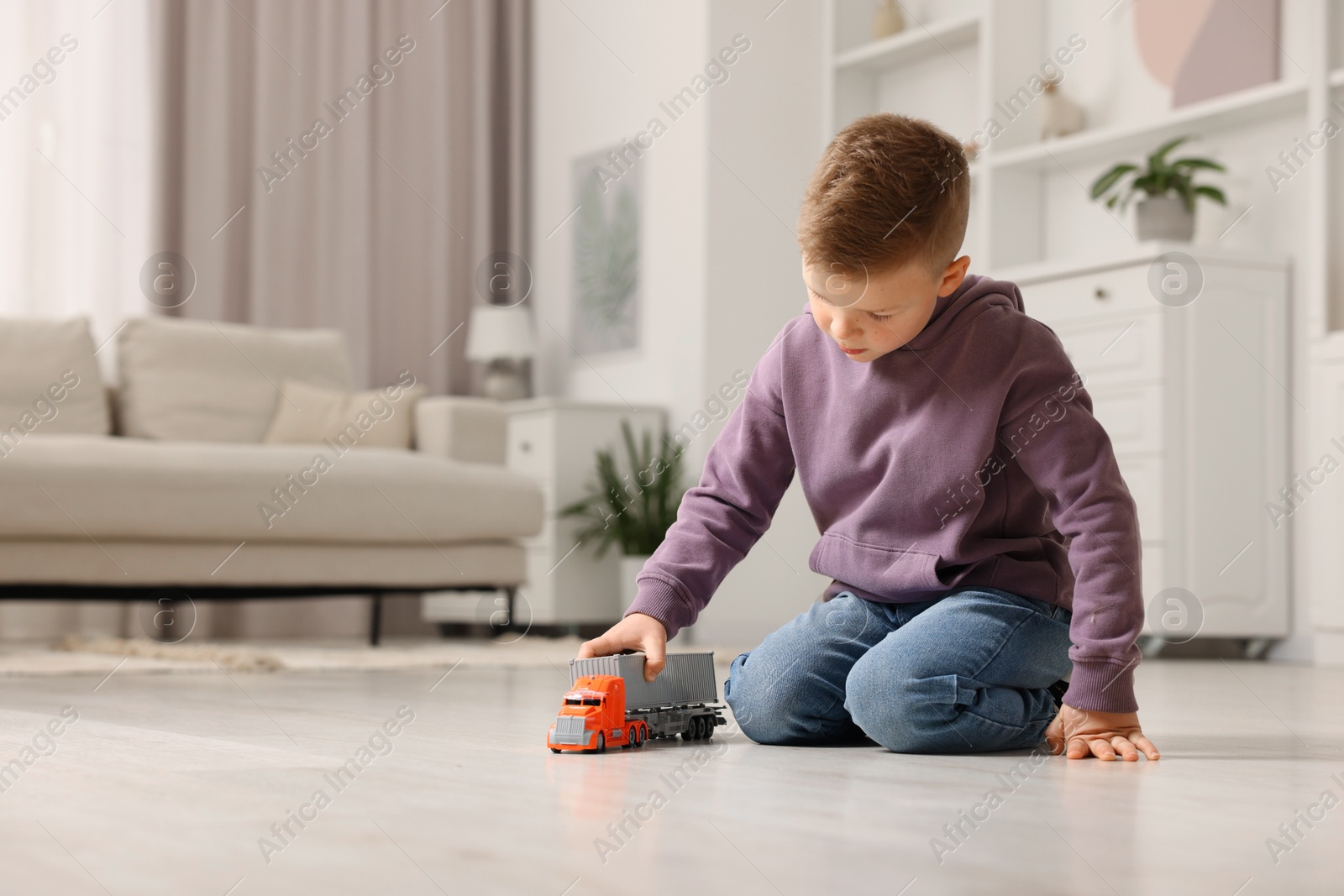 Photo of Little boy playing with toy car at home. Space for text