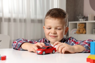 Photo of Little boy playing with toy car at table indoors