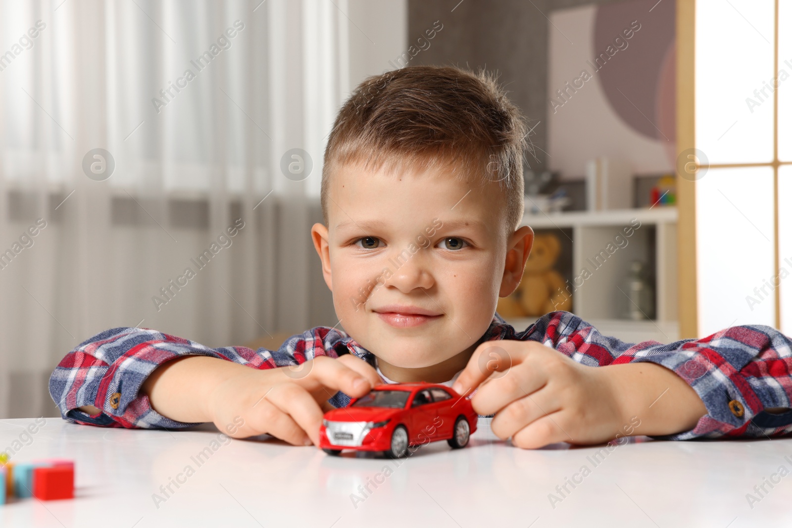 Photo of Little boy playing with toy car at table indoors