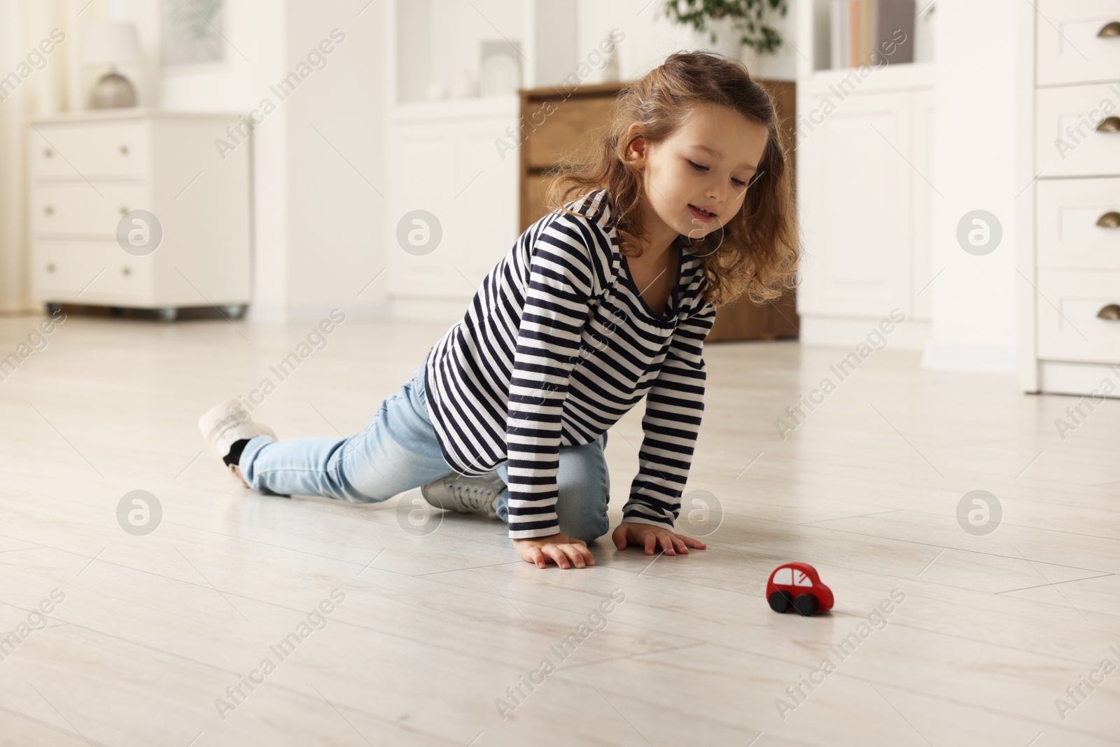 Photo of Little girl playing with toy car on floor at home