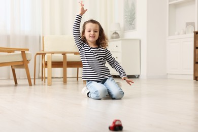 Photo of Little girl playing with toy car on floor at home