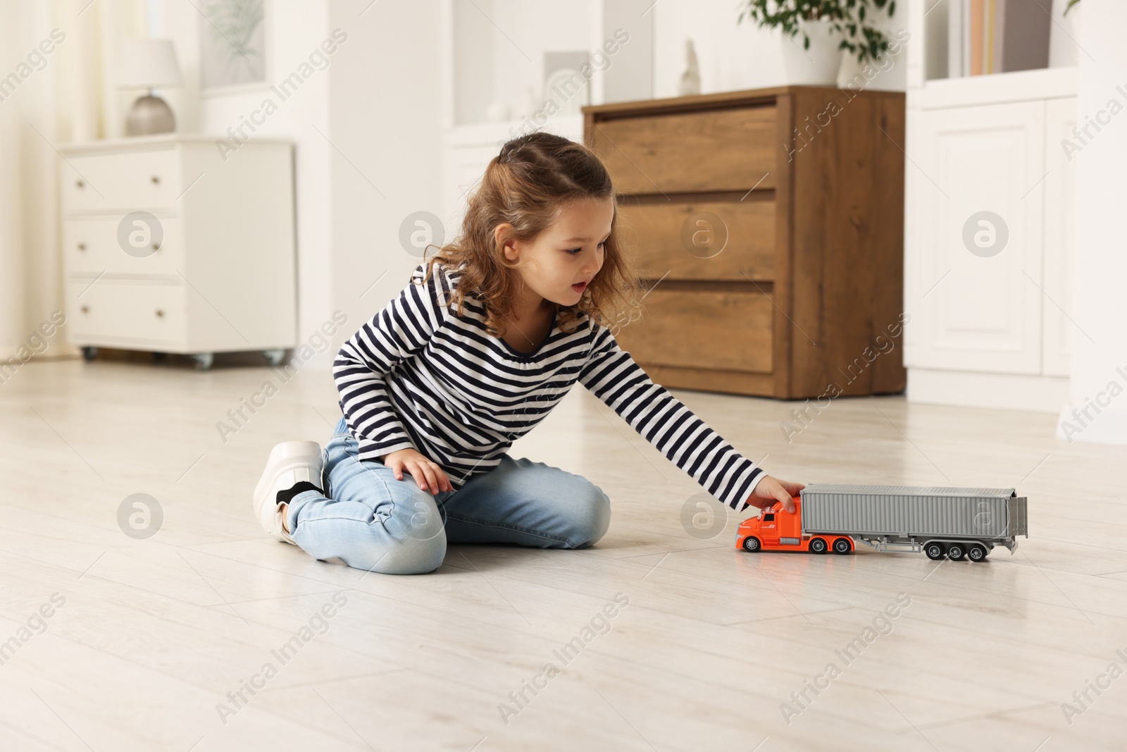 Photo of Little girl playing with toy car on floor at home