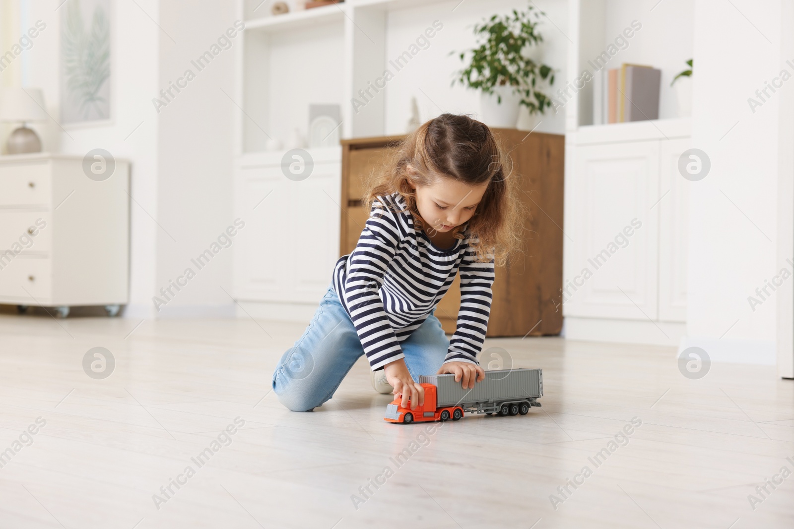 Photo of Little girl playing with toy car on floor at home