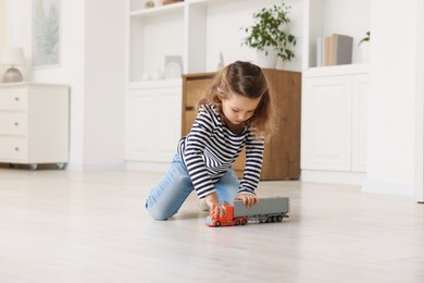 Photo of Little girl playing with toy car on floor at home