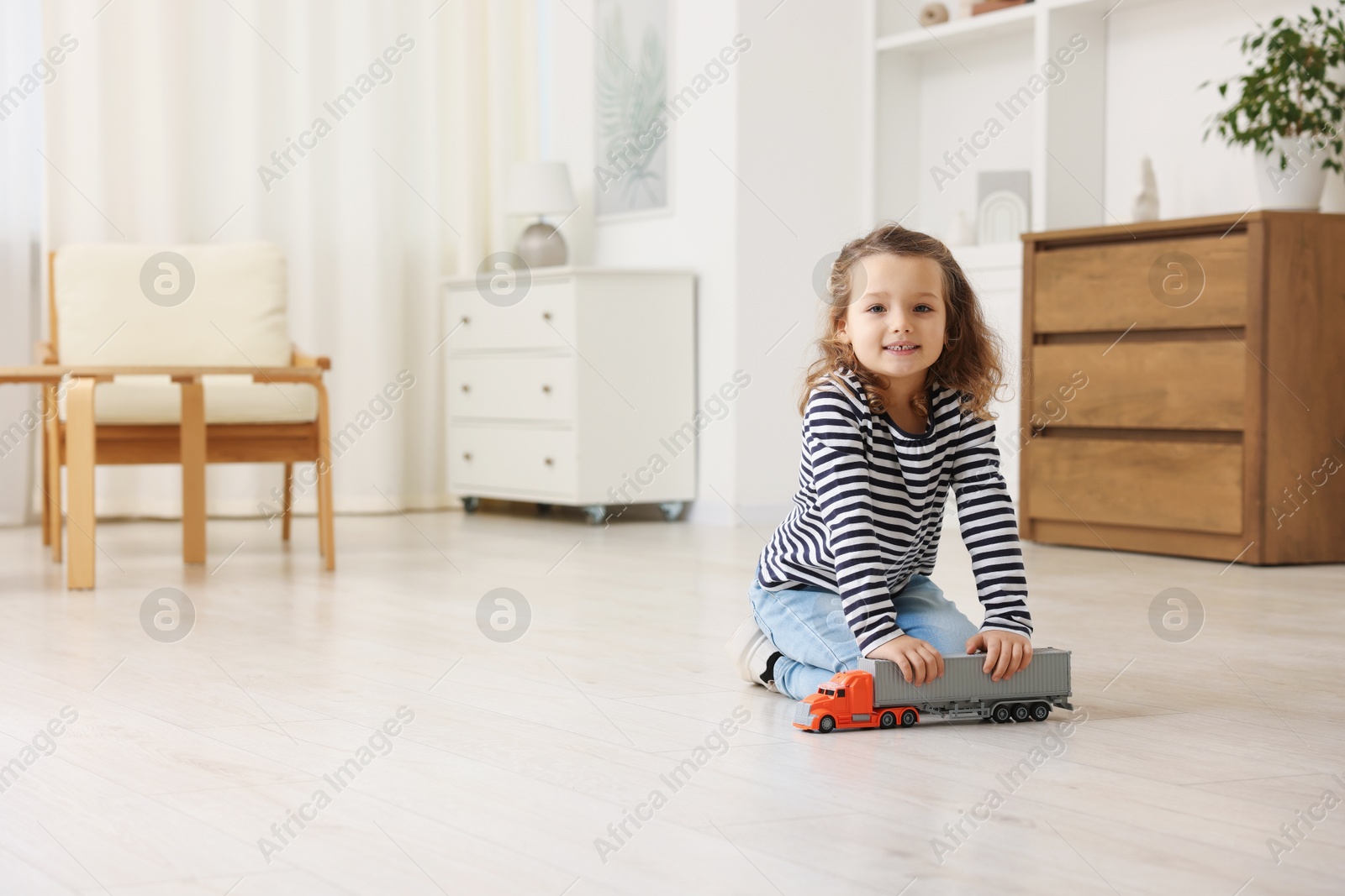 Photo of Little girl playing with toy car on floor at home, space for text