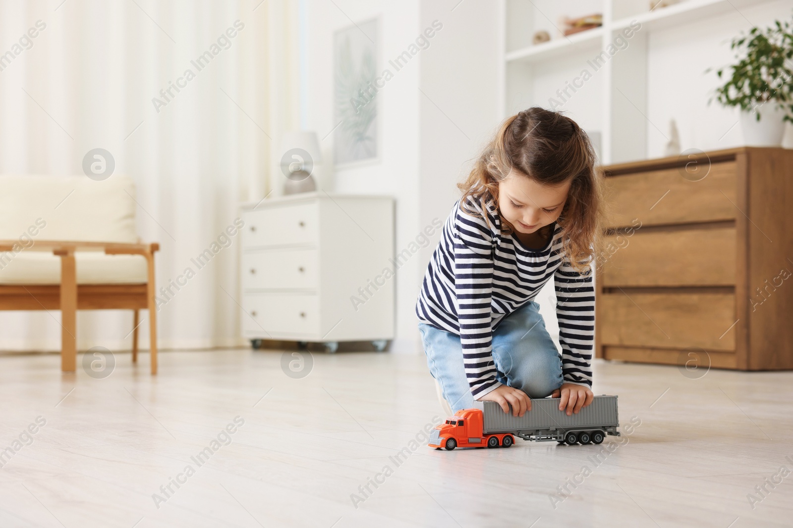 Photo of Little girl playing with toy car on floor at home, space for text