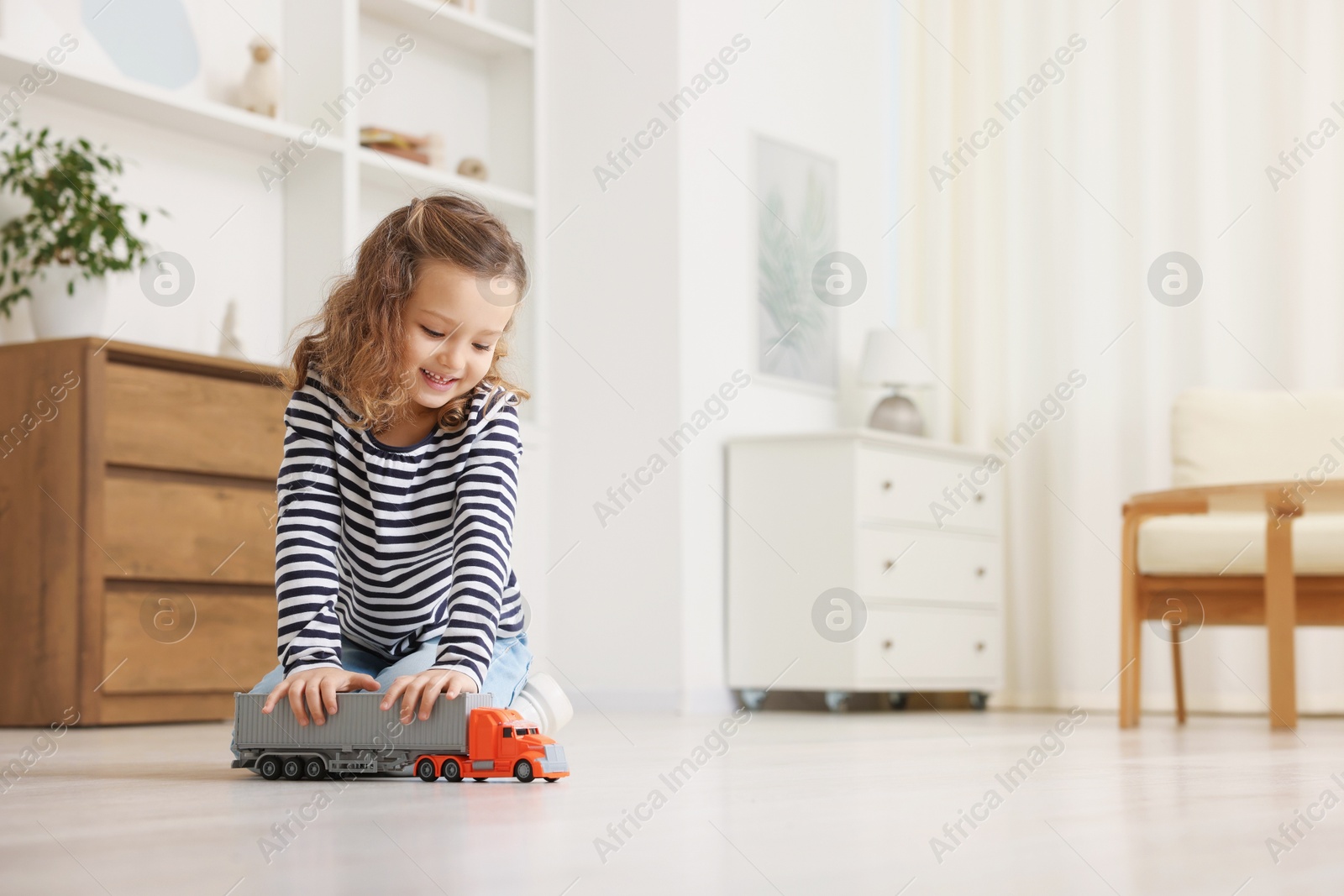 Photo of Little girl playing with toy car on floor at home, space for text