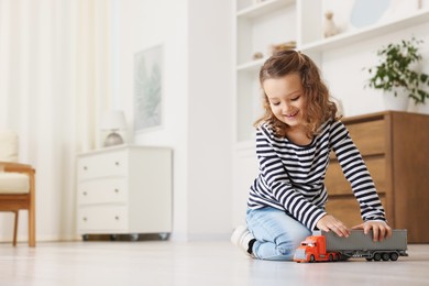 Photo of Little girl playing with toy car on floor at home, space for text