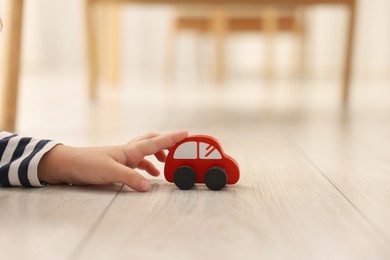 Photo of Little girl playing with toy car on floor at home, closeup. Space for text