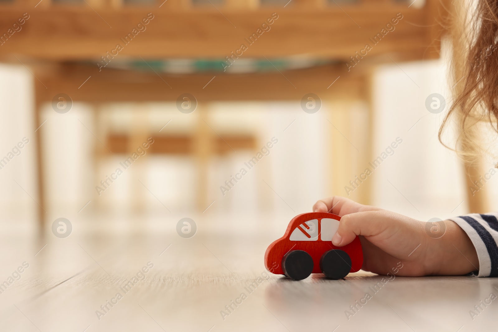 Photo of Little girl playing with toy car on floor at home, closeup. Space for text