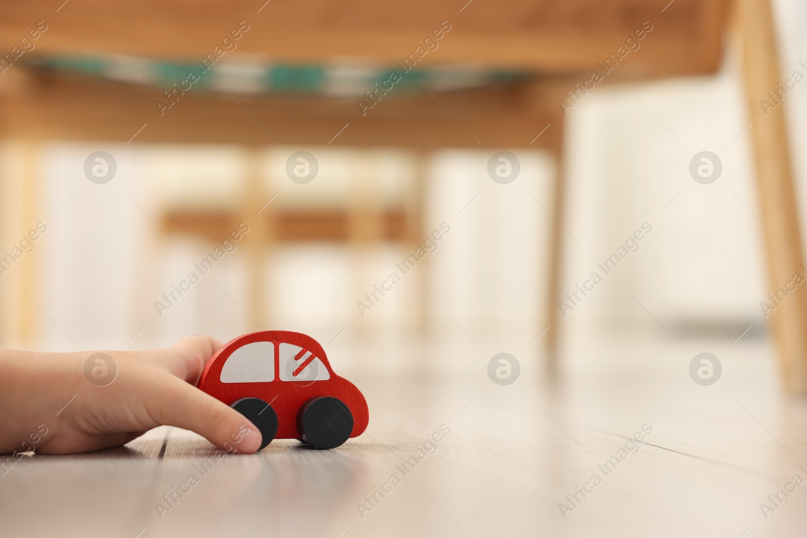 Photo of Little girl playing with toy car on floor at home, closeup. Space for text