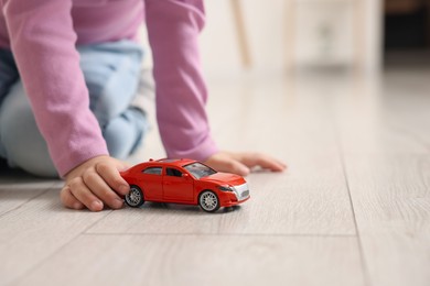 Little girl playing with toy car on floor at home, closeup. Space for text