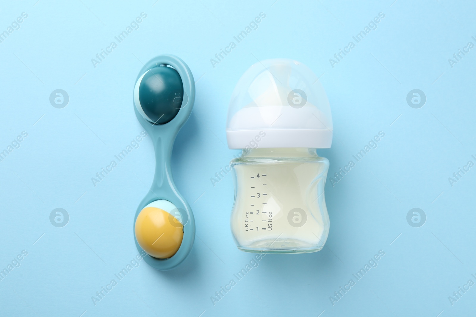 Photo of Feeding bottle with milk and baby rattle on light blue background, flat lay