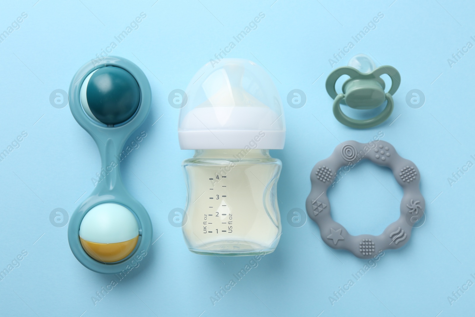 Photo of Feeding bottle with milk, baby rattle, teether and pacifier on light blue background, flat lay