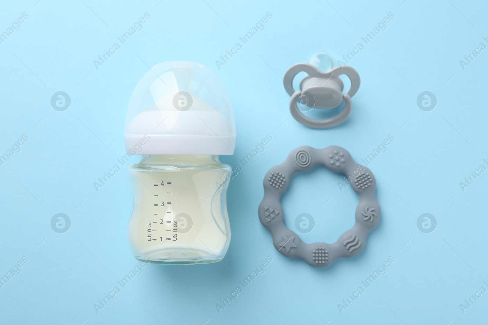 Photo of Feeding bottle with milk, teether and pacifier on light blue background, flat lay