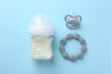 Feeding bottle with milk, teether and pacifier on light blue background, flat lay