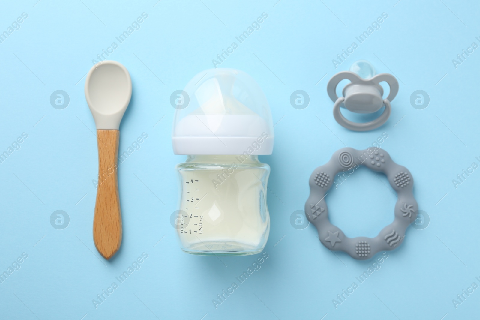 Photo of Feeding bottle with milk, spoon, teether and pacifier on light blue background, flat lay