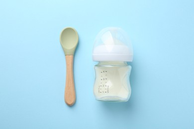 Photo of Feeding bottle with milk and spoon on light blue background, flat lay