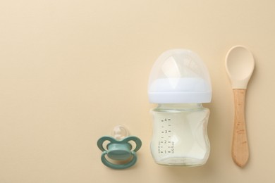 Feeding bottle with milk, pacifier and spoon on beige background, flat lay. Space for text