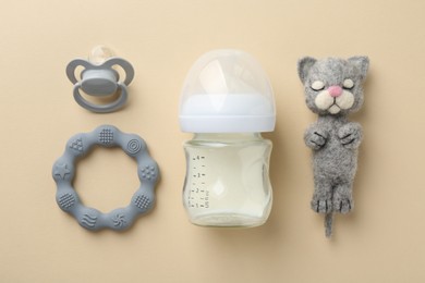 Photo of Feeding bottle with milk, needle felted cat, pacifier and teether on beige background, flat lay