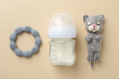 Feeding bottle with milk, needle felted cat and teether on beige background, flat lay