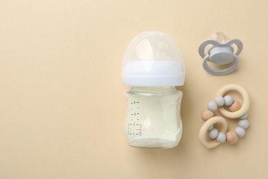 Feeding bottle with milk, pacifier and teether on beige background, flat lay. Space for text