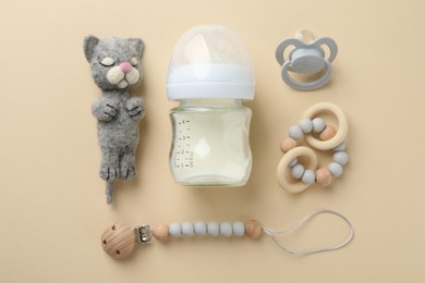 Photo of Feeding bottle with milk, needle felted cat, pacifier and teethers on beige background, flat lay