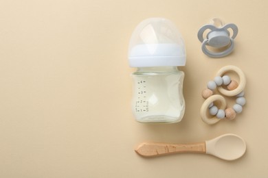 Feeding bottle with milk, pacifier, teether and spoon on beige background, flat lay. Space for text