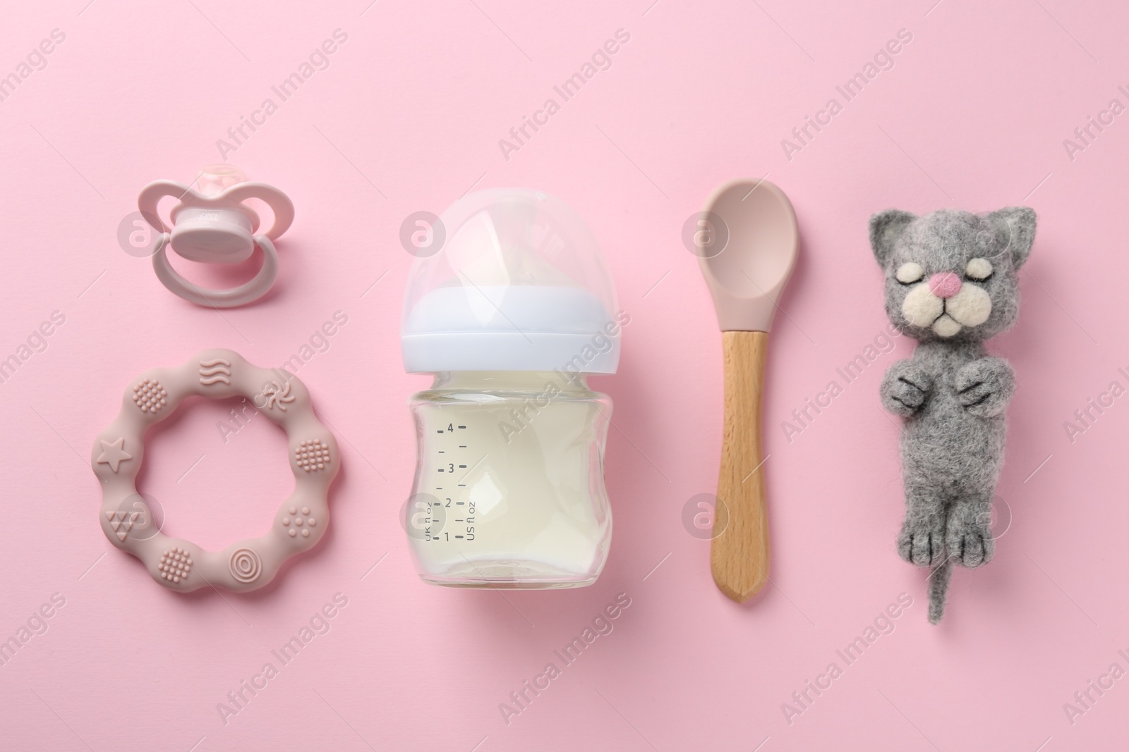 Photo of Feeding bottle with milk, needle felted cat, spoon, pacifier and teether on pink background, flat lay