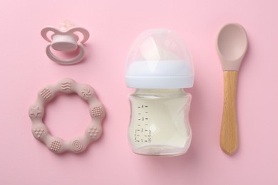 Feeding bottle with milk, spoon, pacifier and teether on pink background, flat lay